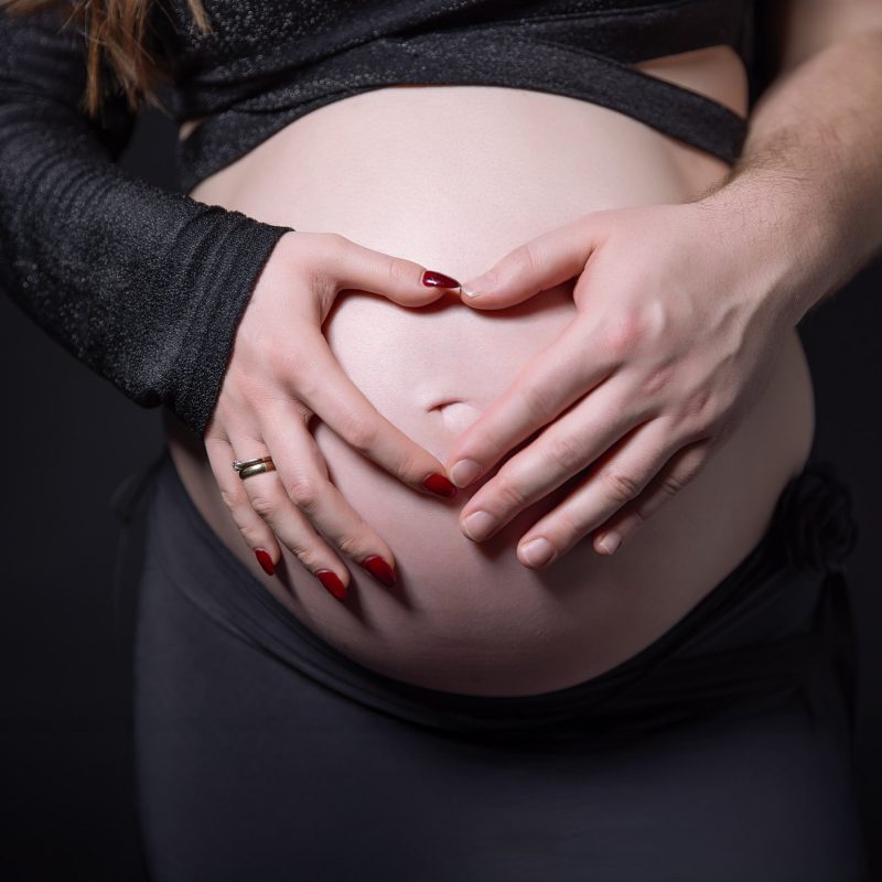 Ręce na brzuchu ciążowym kobiety i mężczyzny w układzie serca