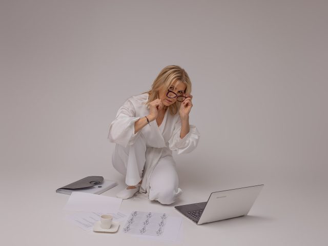 kobieta na białym tle w białym ubraniu w ciemnych okularach patrzy w laptopa